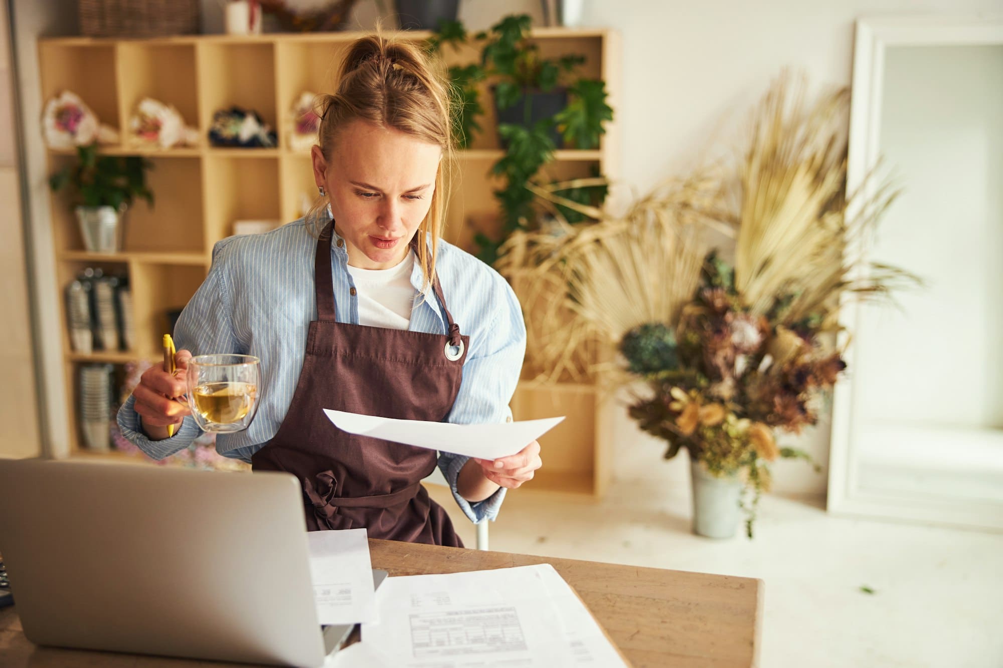 Woman at the laptop scrutinizing an invoice in her hand